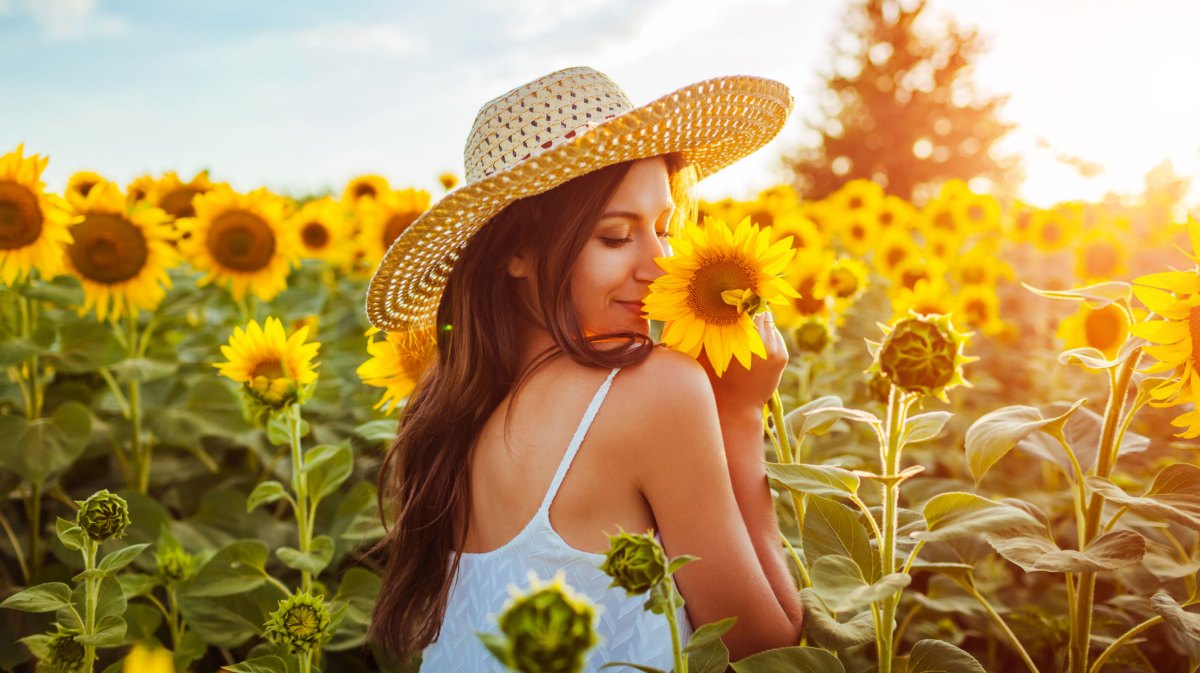 Frau mit Strohhut im Sonnenblumenfeld