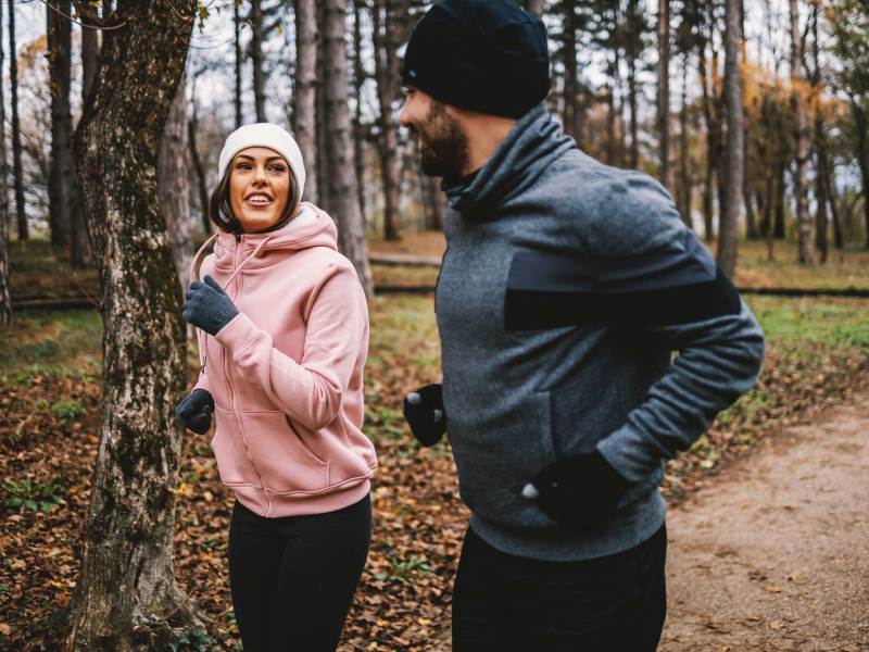 Paar mit Mütze und Handschuhen, das im Herbst im Wald läuft und sich erholt, Konzept für gesundes Leben.