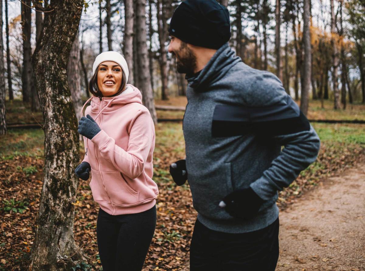 Paar mit Mütze und Handschuhen, das im Herbst im Wald läuft und sich erholt, Konzept für gesundes Leben.