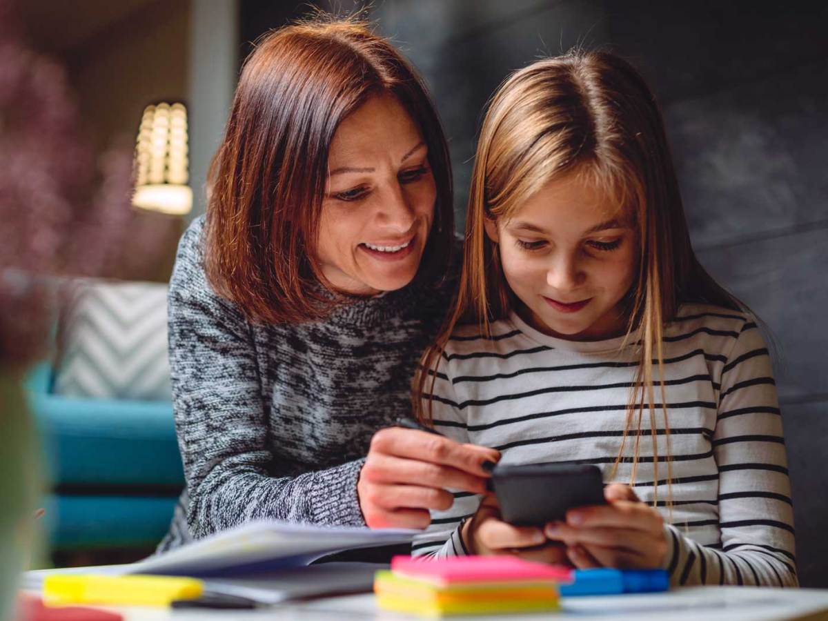 Mutter und Tochter sitzen am Tisch und schauen gemeinsam ins Handy.