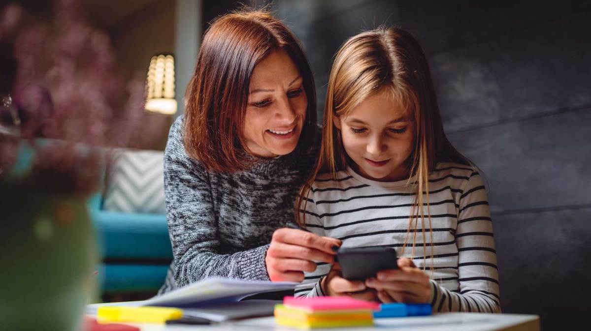 Mutter und Tochter sitzen am Tisch und schauen gemeinsam ins Handy.