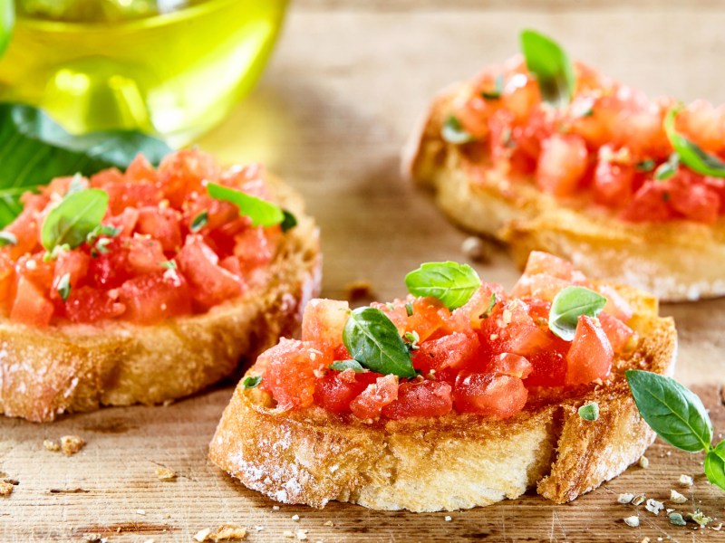 Drei Scheiben Brot mit Bruschetta neben einer Flasche Olivenöl.