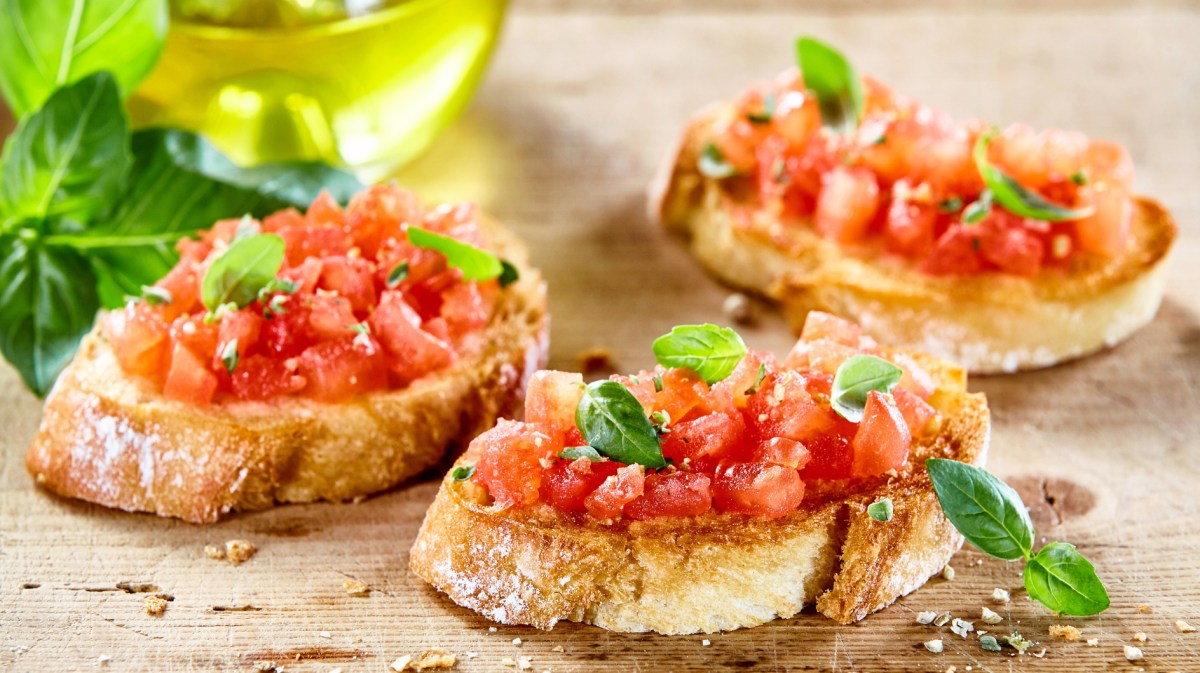 Drei Scheiben Brot mit Bruschetta neben einer Flasche Olivenöl.