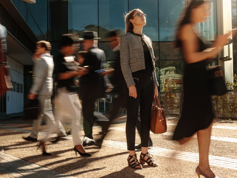 Frau in Businesskleidung steht zwischen Menschen, die sich schnell bewegen.