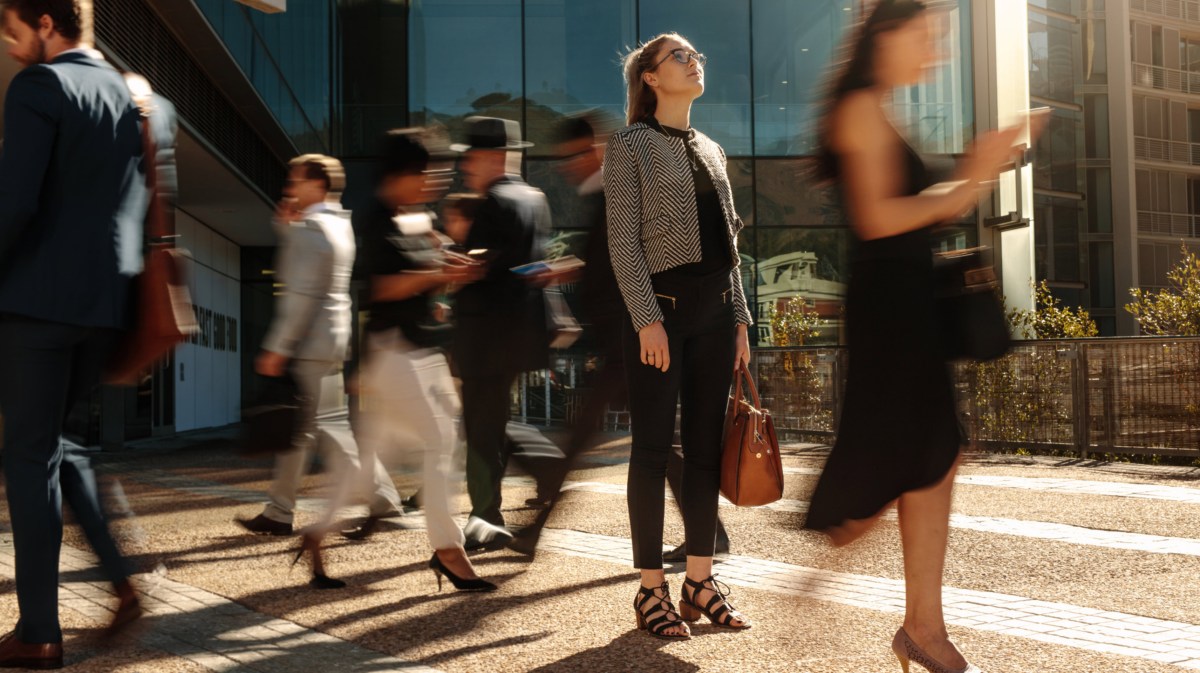 Frau in Businesskleidung steht zwischen Menschen, die sich schnell bewegen.