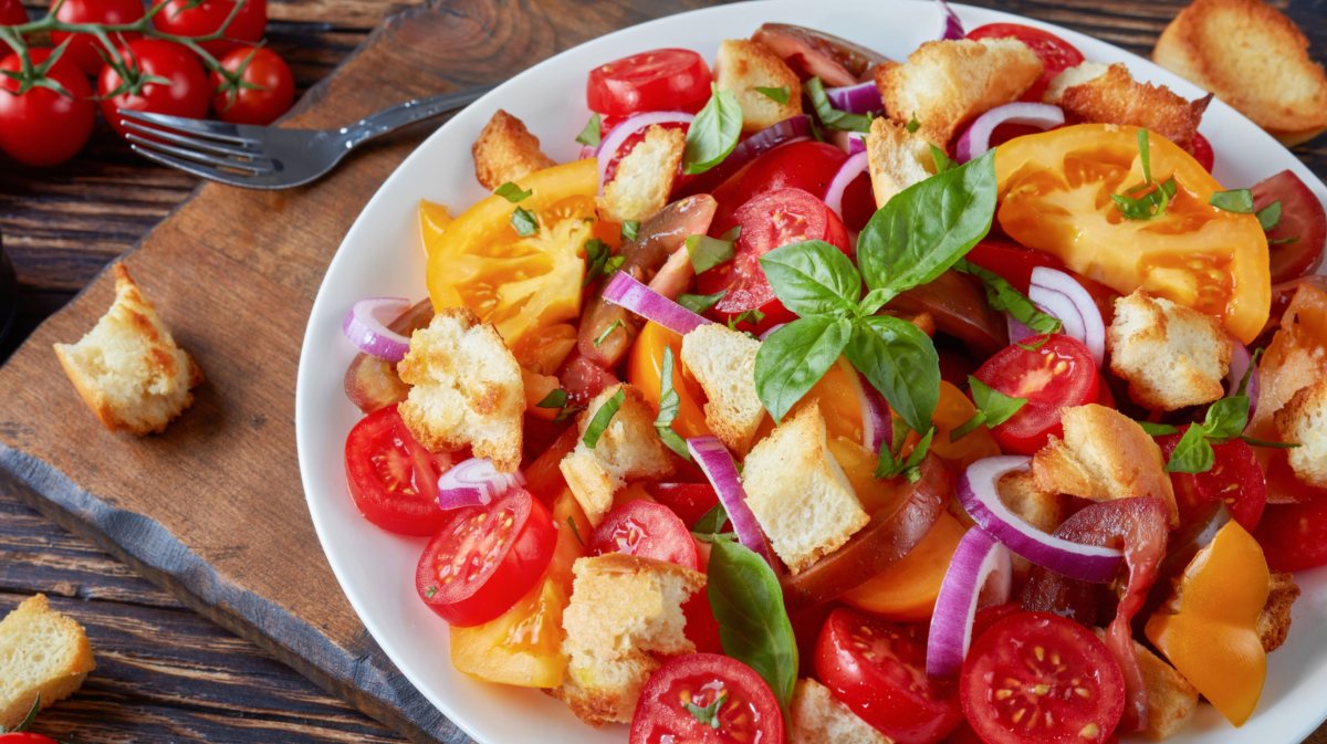 Brotsalat nach italienischer Art mit Tomaten, roten Zwiebeln und Basilikum in einer weißen Schüssel.