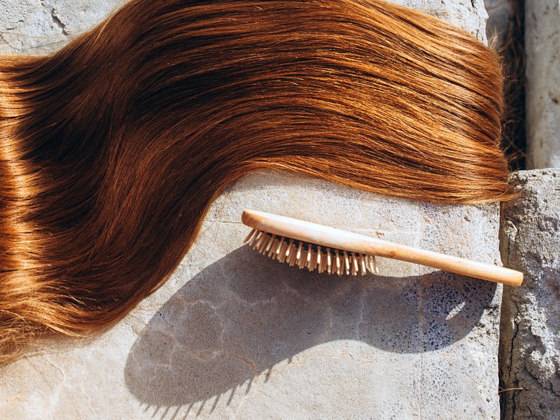 Glänzendes rotes Haar liegt in einer Welle daneben eine Haarbürste auf Steinboden