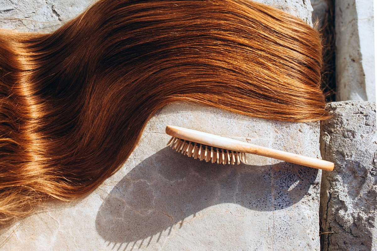 Glänzendes rotes Haar liegt in einer Welle daneben eine Haarbürste auf Steinboden