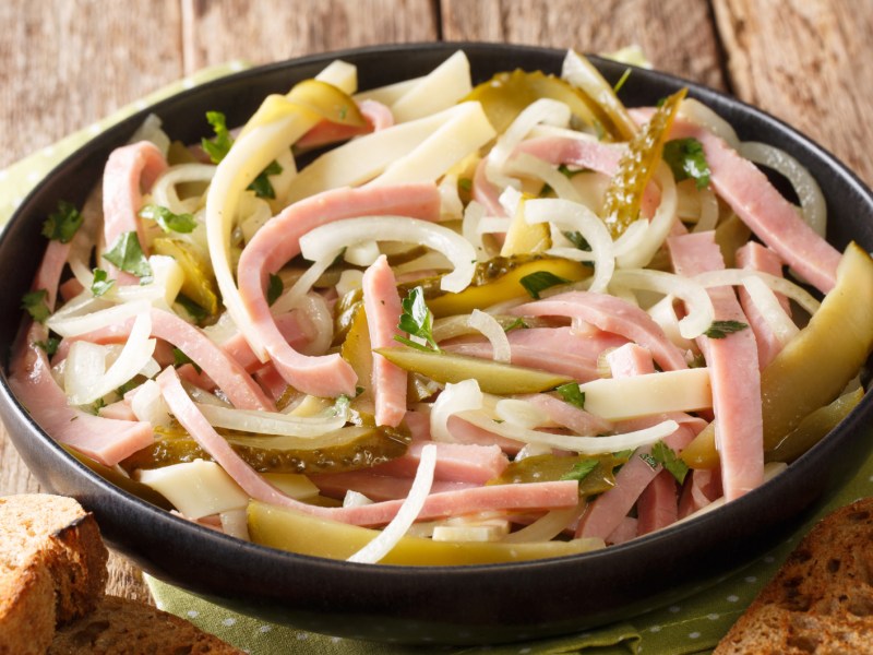 Wurstsalat mit Zwiebeln und Gurken in schwarzer Schüssel.