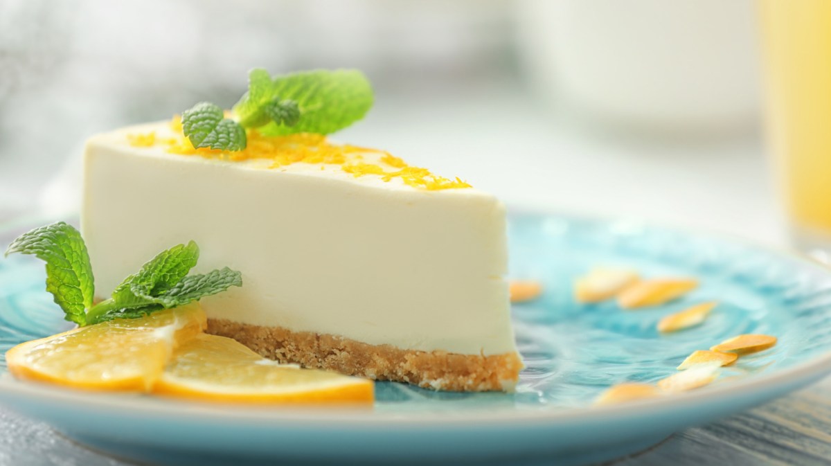 Frischkäse-Zitronen-Torte mit Keksboden auf einem türkisen Teller.