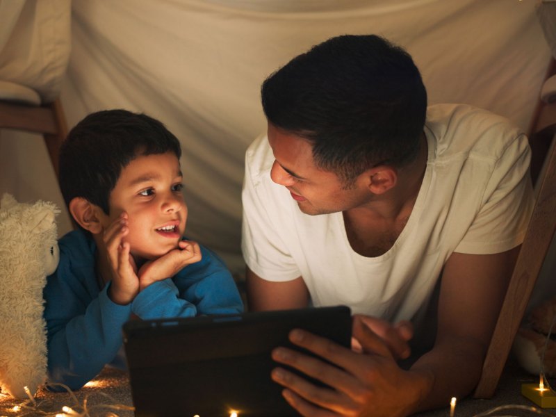 Vater und Sohn liegen am Abend bei indirektem Licht in einer kleinen, selbstgebauten Höhle und sprechen angeregt miteinander.