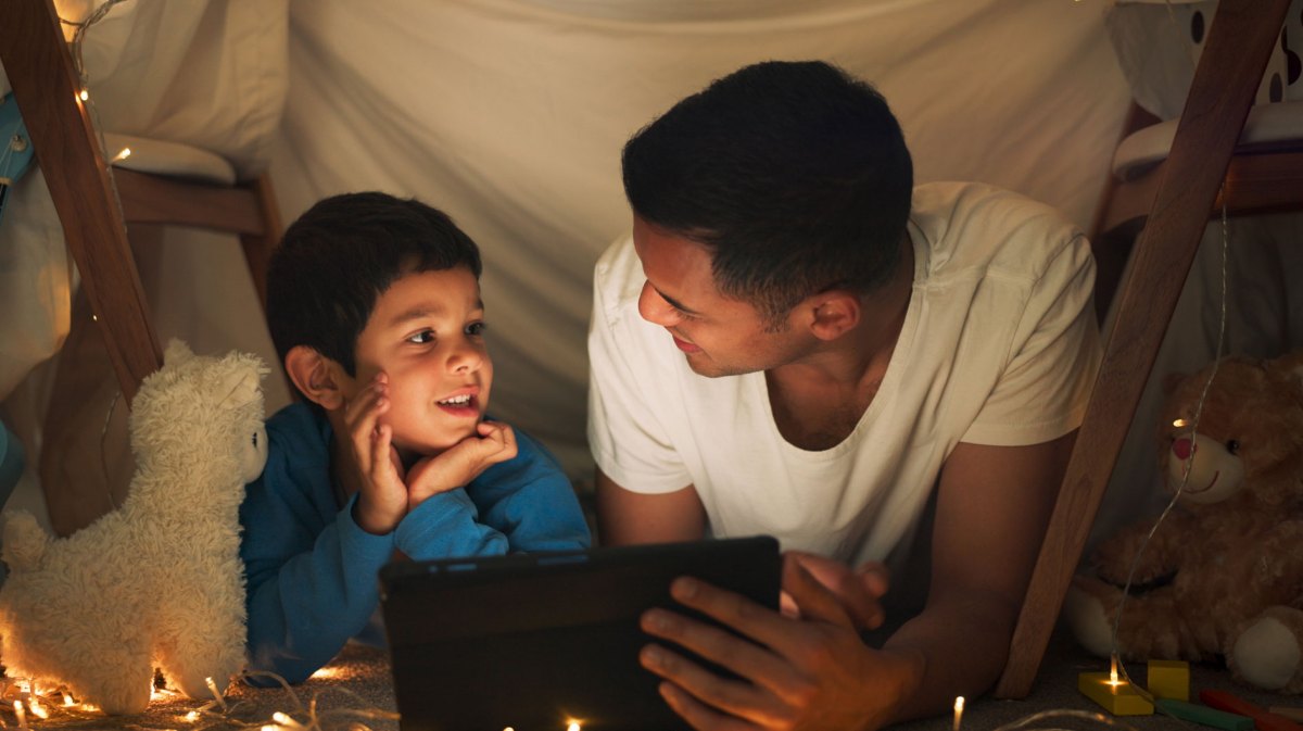 Vater und Sohn liegen am Abend bei indirektem Licht in einer kleinen, selbstgebauten Höhle und sprechen angeregt miteinander.