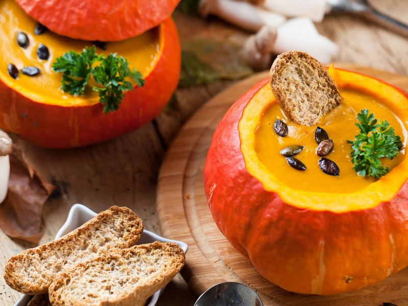 Kürbissuppe angerichtet in einem Hokkaidokürbis mit Brot und Salz daneben