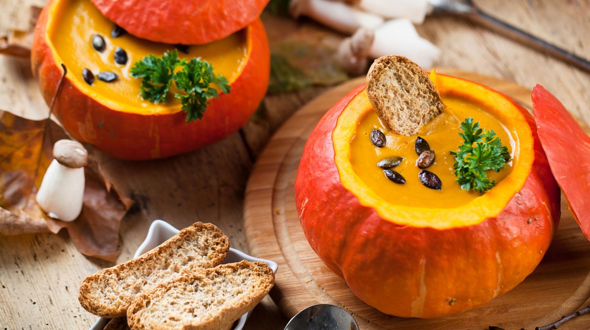 Kürbissuppe angerichtet in einem Hokkaidokürbis mit Brot und Salz daneben