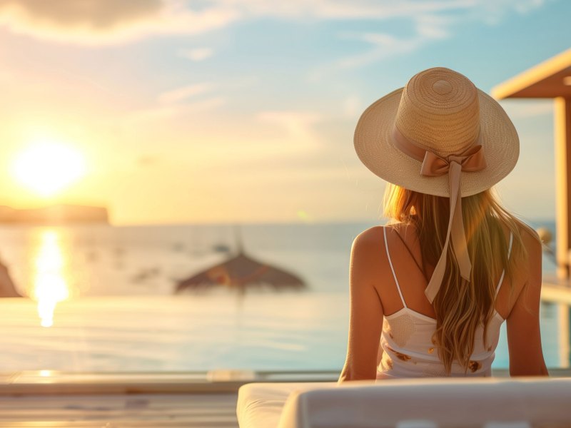 Frau mit Sonnenhut sitzt im Infinitypool und schaut Sonnenuntergang