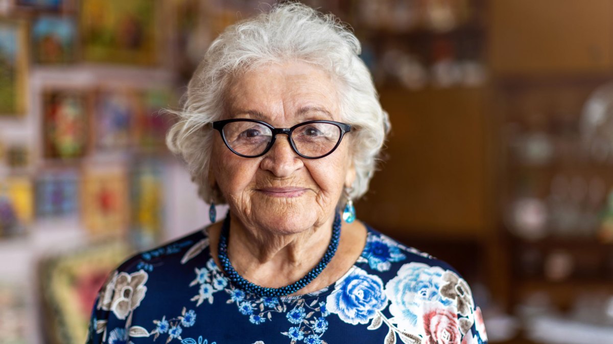 Porträt einer alten Frau, die freundlich in die Kamer lächelt.