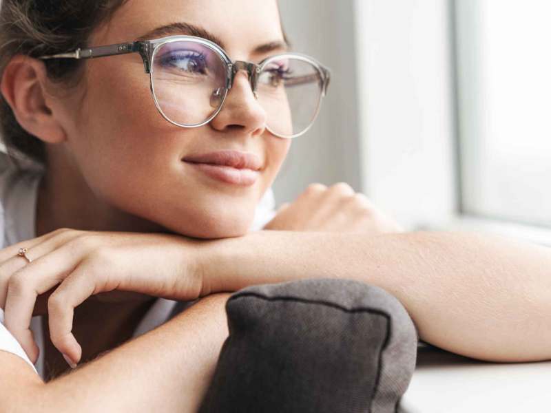 Junge Frau mit Brille guckt zufrieden aus dem Fenster.