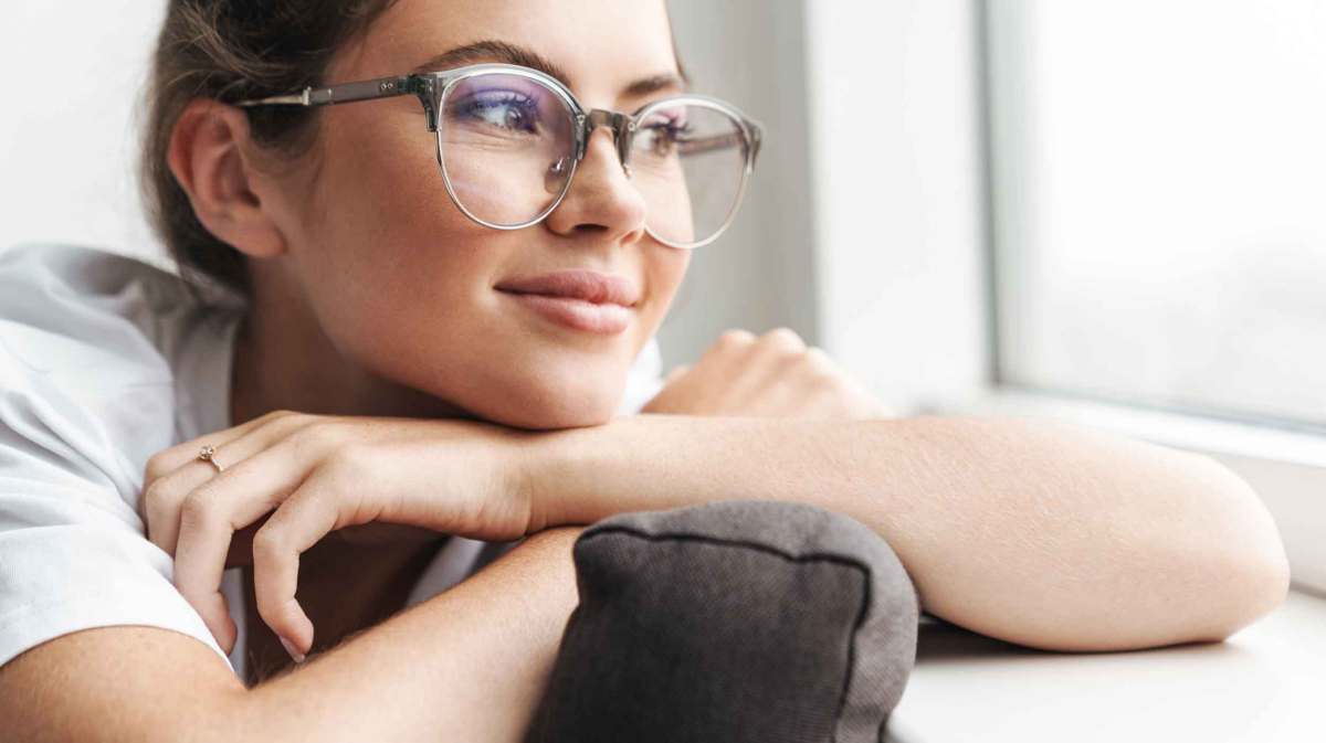 Junge Frau mit Brille guckt zufrieden aus dem Fenster.