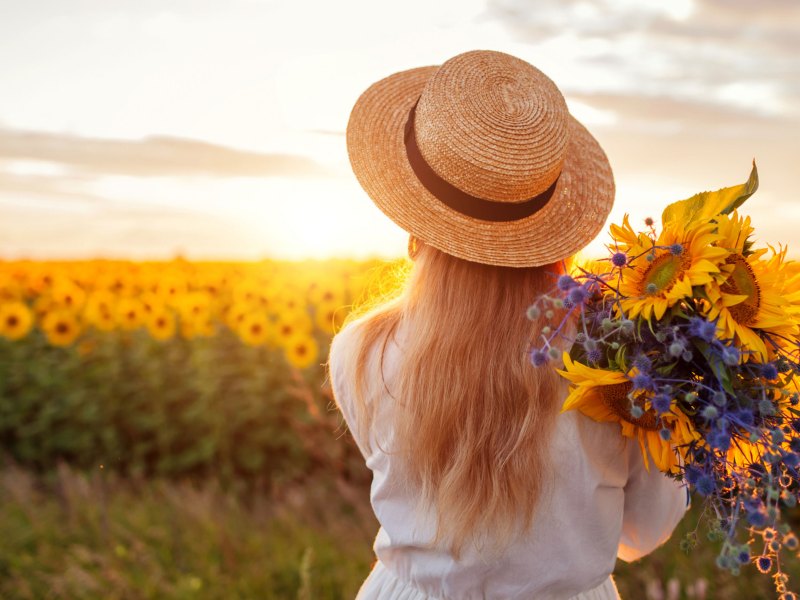 Frau mit Strohhut auf einem Sonnenblumenfeld