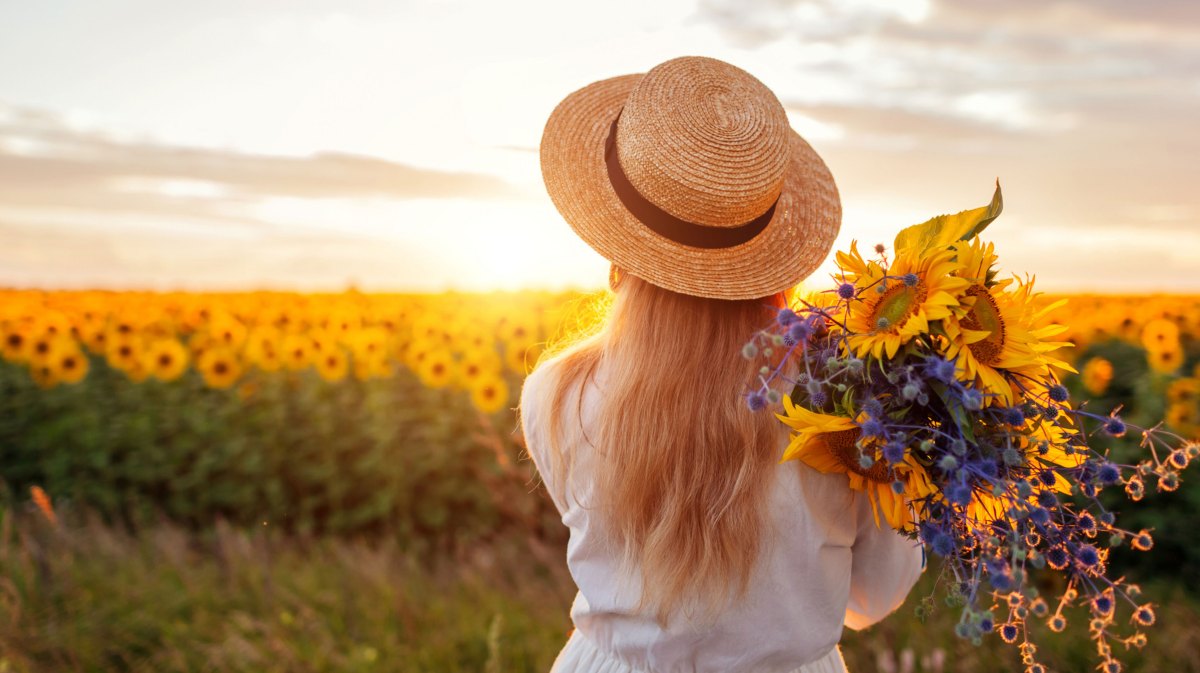 Frau mit Strohhut auf einem Sonnenblumenfeld