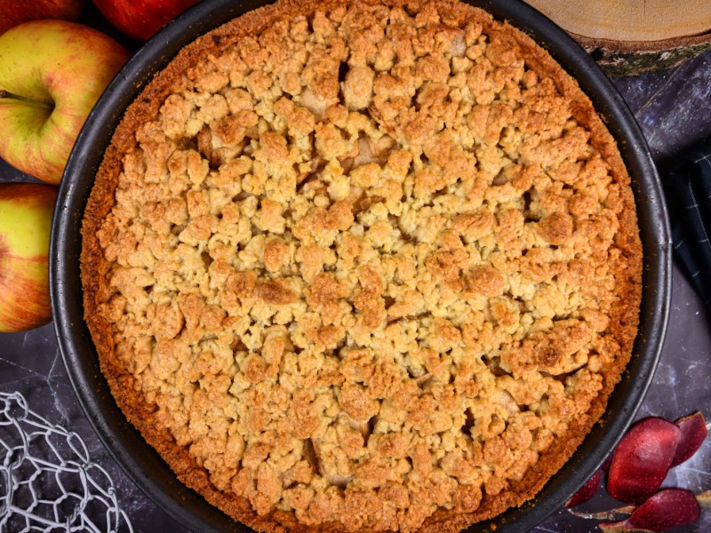 Apfelkuchen mit Streusel von oben, daneben liegen Äpfel.