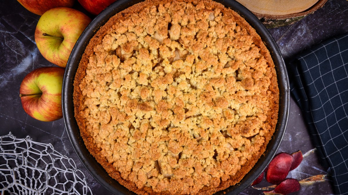 Apfelkuchen mit Streusel von oben, daneben liegen Äpfel.