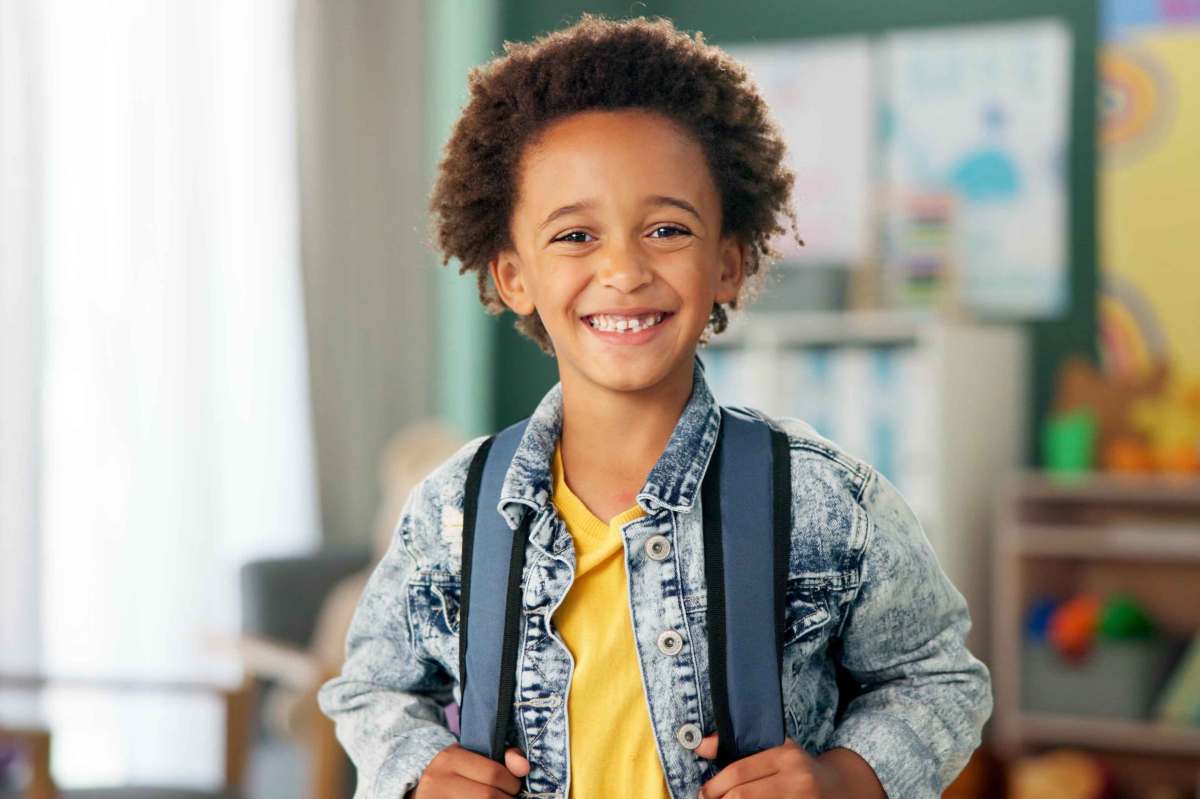 Porträt eines Jungen, der im Klassenzimmer steht und in die Kamera strahlt.