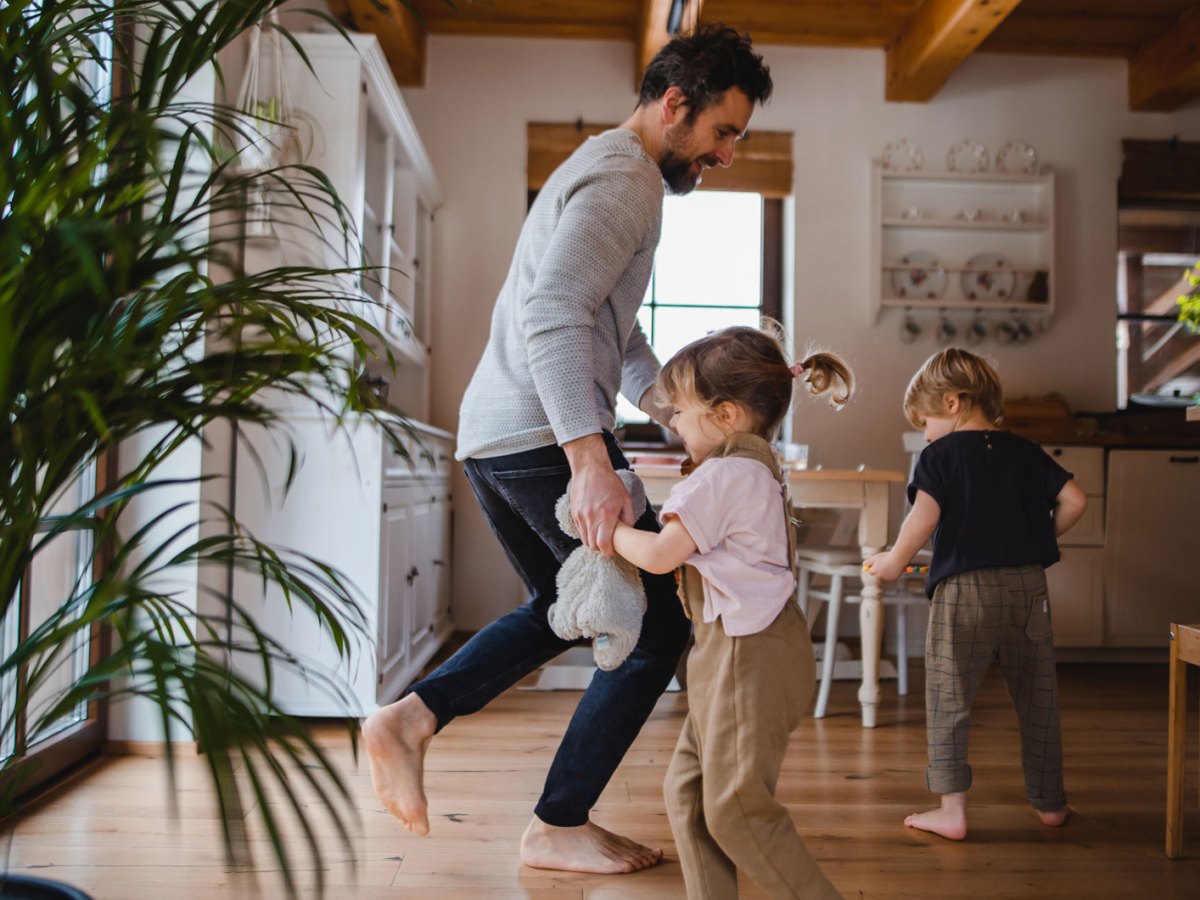 Vater tanzt mit seinen beiden Kindern in einer Wohnung im skandinavischen Stil.