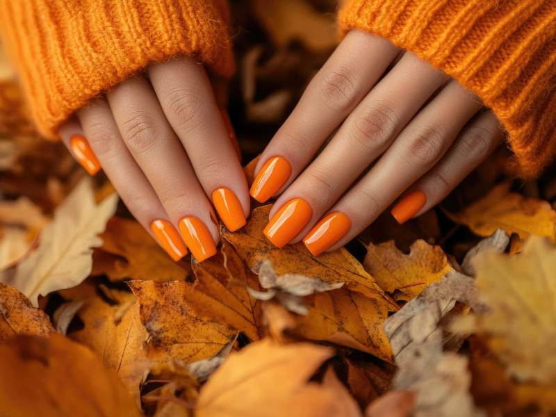 Weibliche Hände mit kräftiger orangefarbener Maniküre, die einen Strauß gefallener Herbstblätter aufheben, wobei die leuchtende Nagelfarbe die warmen Farbtöne der Jahreszeit ergänzt Generiert mit AI