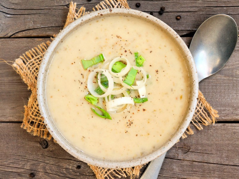 Kartoffelsuppe mit Lauch in einer hellen Schüssel auf einem Holztisch.