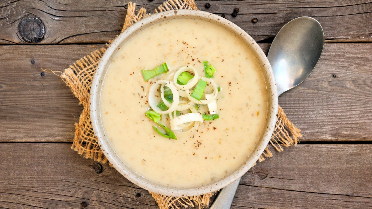 Kartoffelsuppe mit Lauch in einer hellen Schüssel auf einem Holztisch.