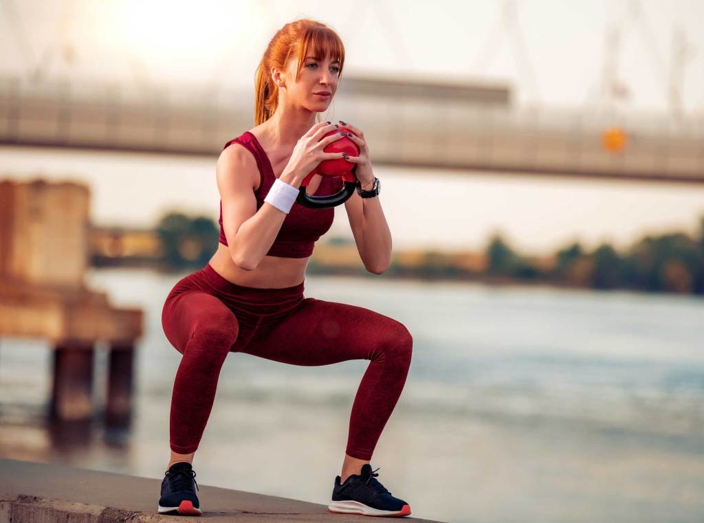 Sportliche Frau macht draußen Kettlebell Squats