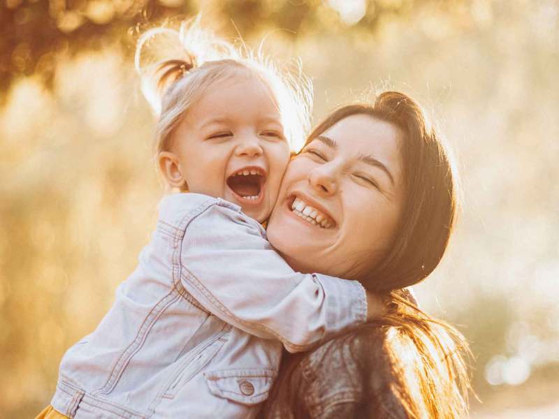 Mutter trägt ihre Tochter im Arm und lacht.