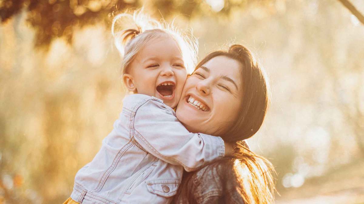 Mutter trägt ihre Tochter im Arm und lacht.