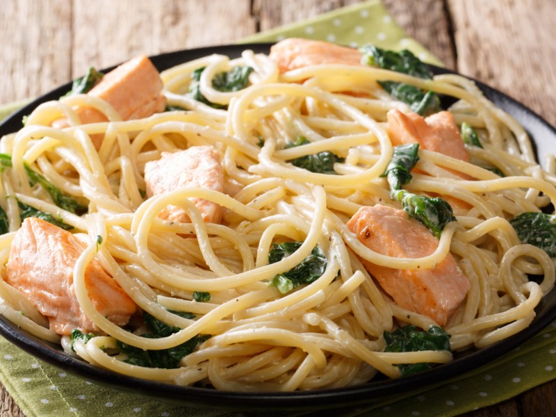 Spaghetti mit Lachs und Spinat in einer schwarzen Schüssel.