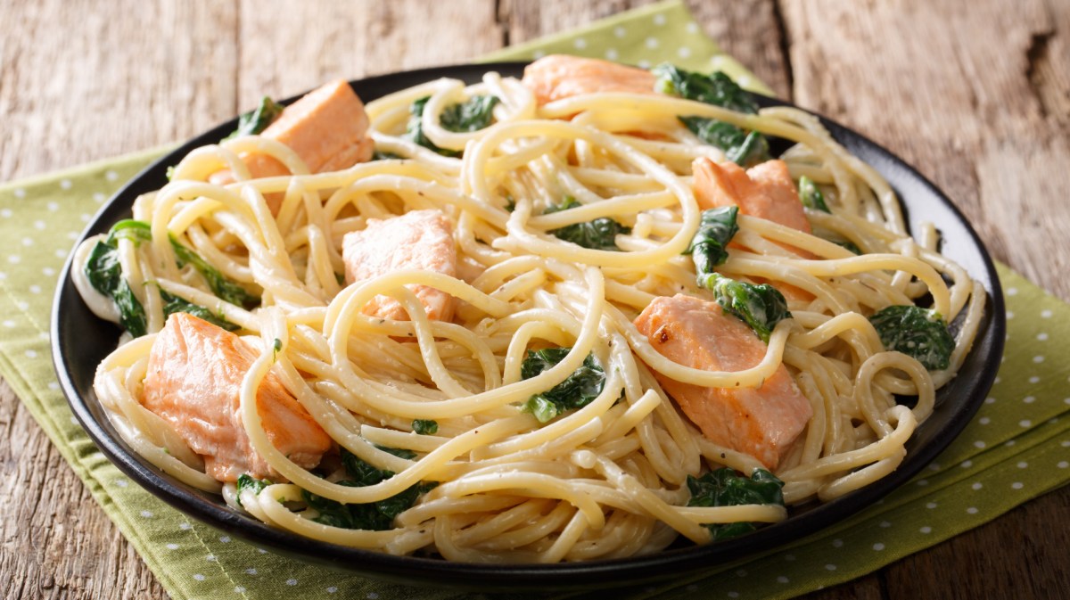 Spaghetti mit Lachs und Spinat in einer schwarzen Schüssel.