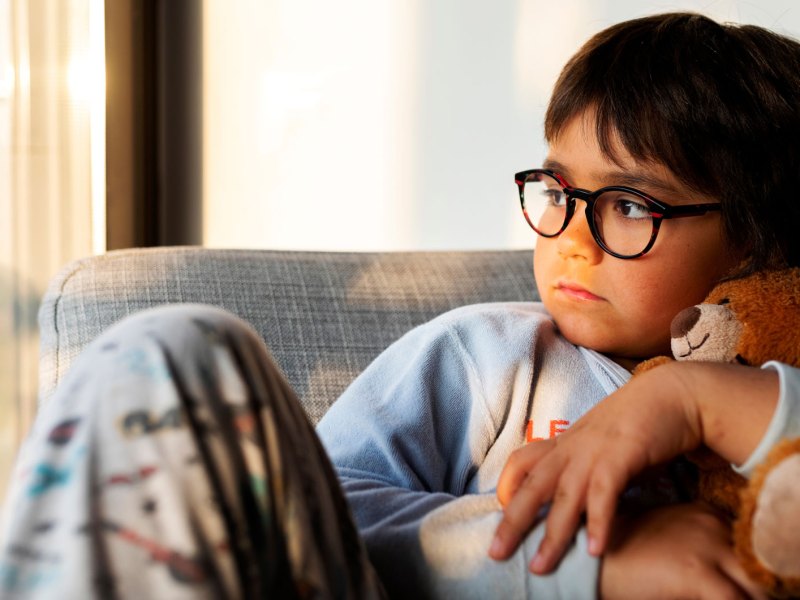 Porträt eines Jungen, ca. 10 Jahre alt, der mit einem Teddy im Arm melancholisch aus dem Fenster schaut.