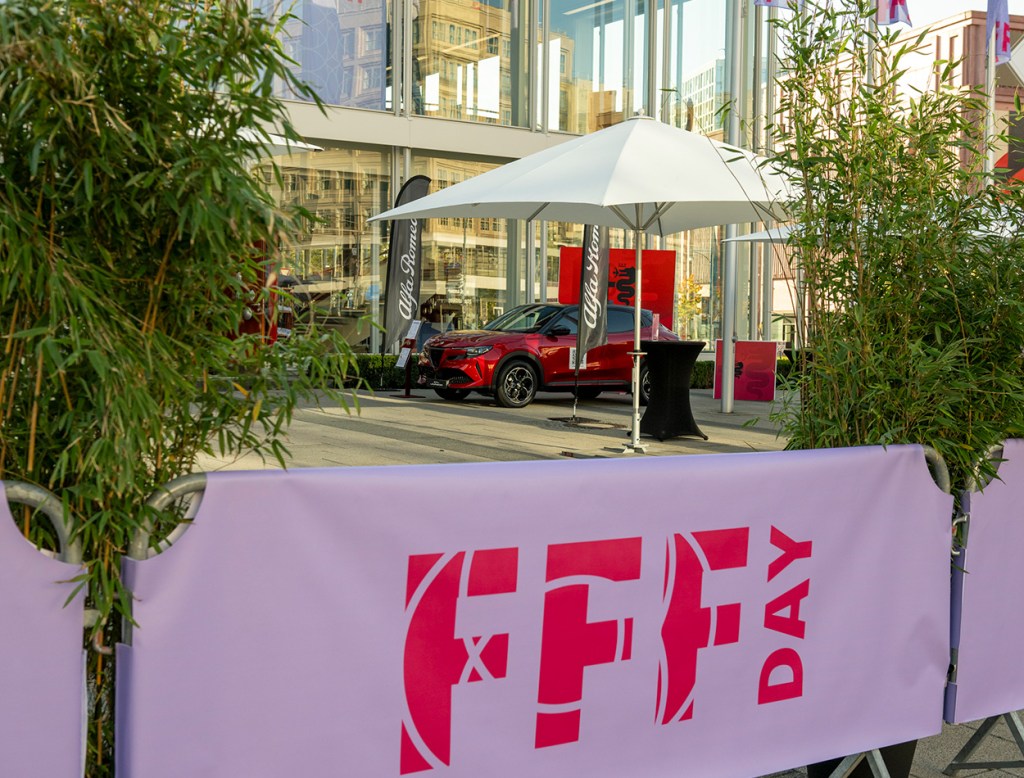 Ein rotes Auto vor einer Glasfassade, umgeben von Bambuspflanzen, mit einem lila Banner mit der Aufschrift "FFF Day" im Vordergrund