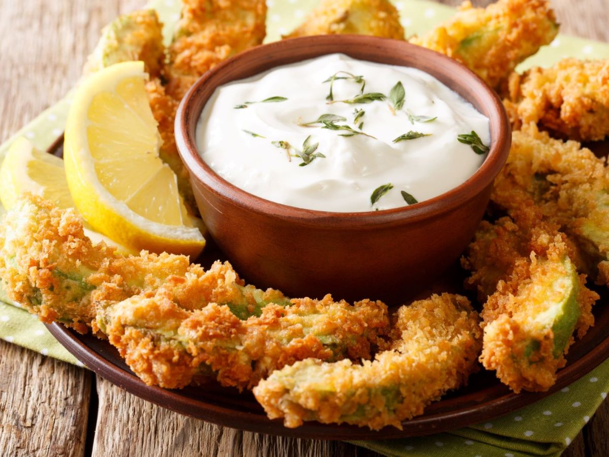 Frittierte Avocado-Stücke mit Dip auf einer Platte angerichtet.