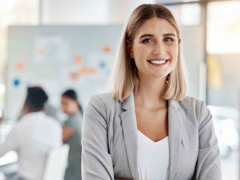 Junge Frau mit Blazer lächelt im Büro.