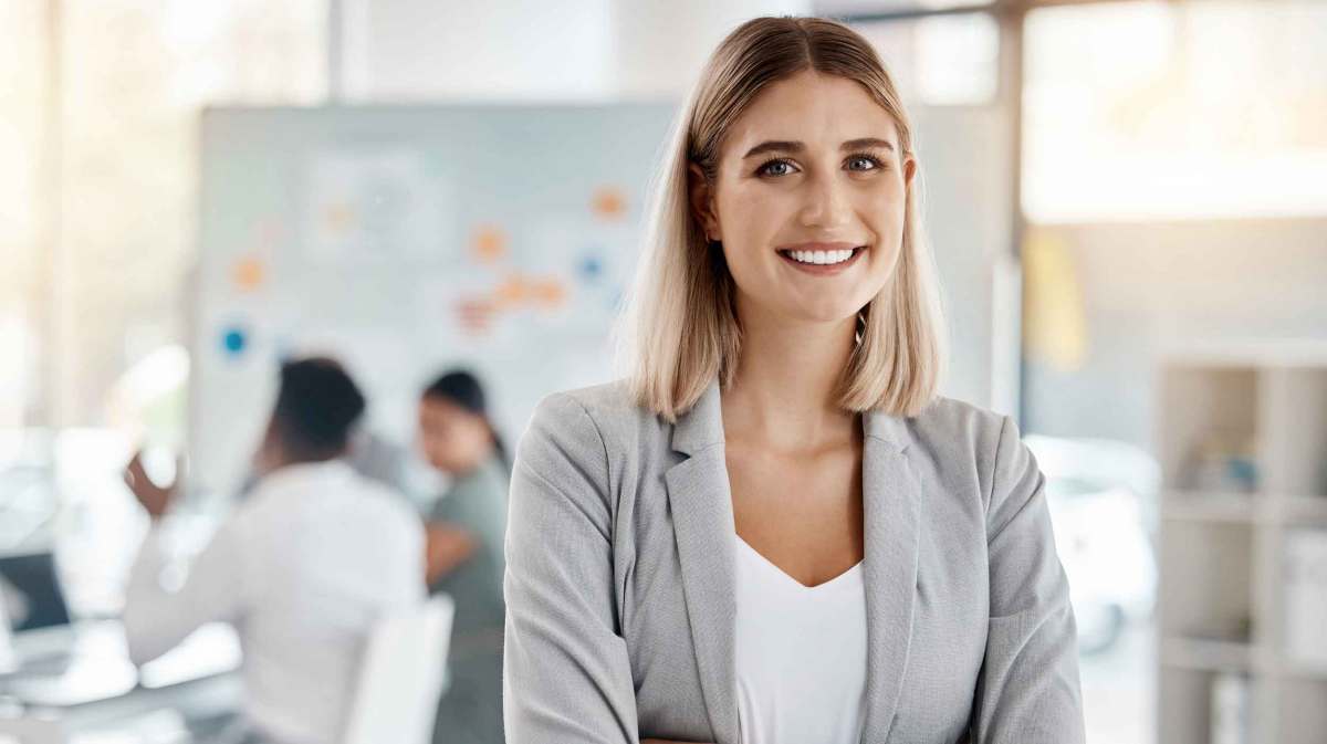 Junge Frau mit Blazer lächelt im Büro.