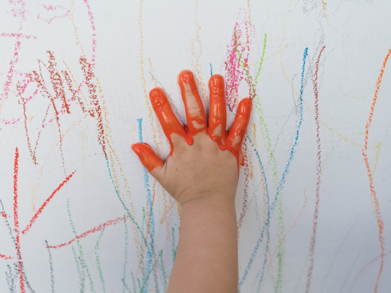 Kinderhand mit roter Farbe als Symbolbild für Flecken auf weißer Wand entfernen