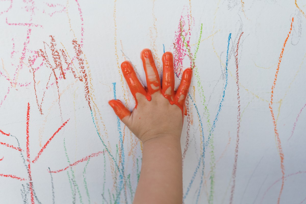 Kinderhand mit roter Farbe als Symbolbild für Flecken auf weißer Wand entfernen