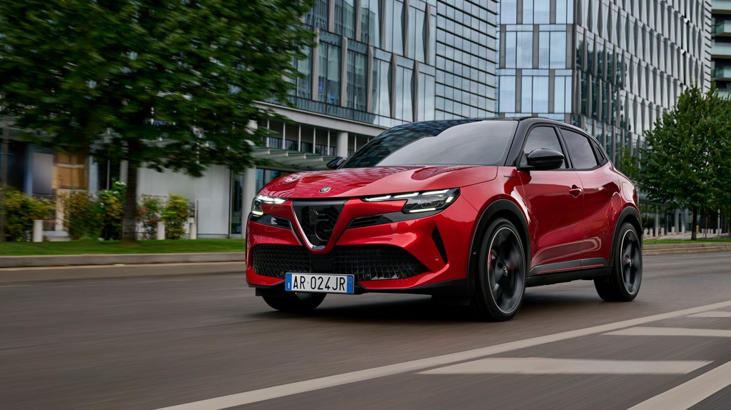 Ein roter SUV fährt dynamisch auf einer leeren Stadtstraße, moderne Bürogebäude und Bäume ziehen im Hintergrund vorbei.