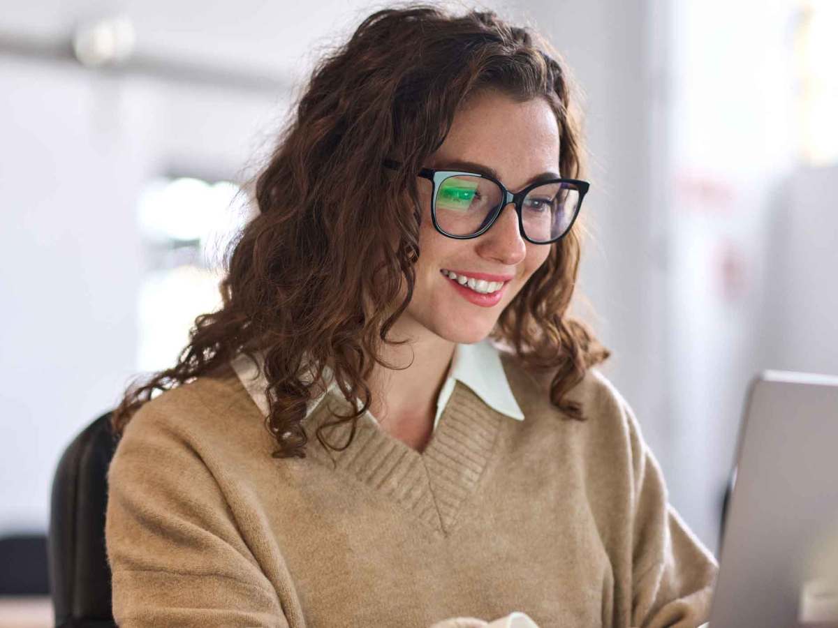 Frau mit braunen Locken und Brille sitzt vor dem Laptop.