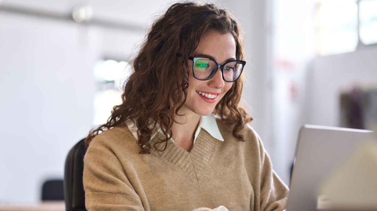 Frau mit braunen Locken und Brille sitzt vor dem Laptop.