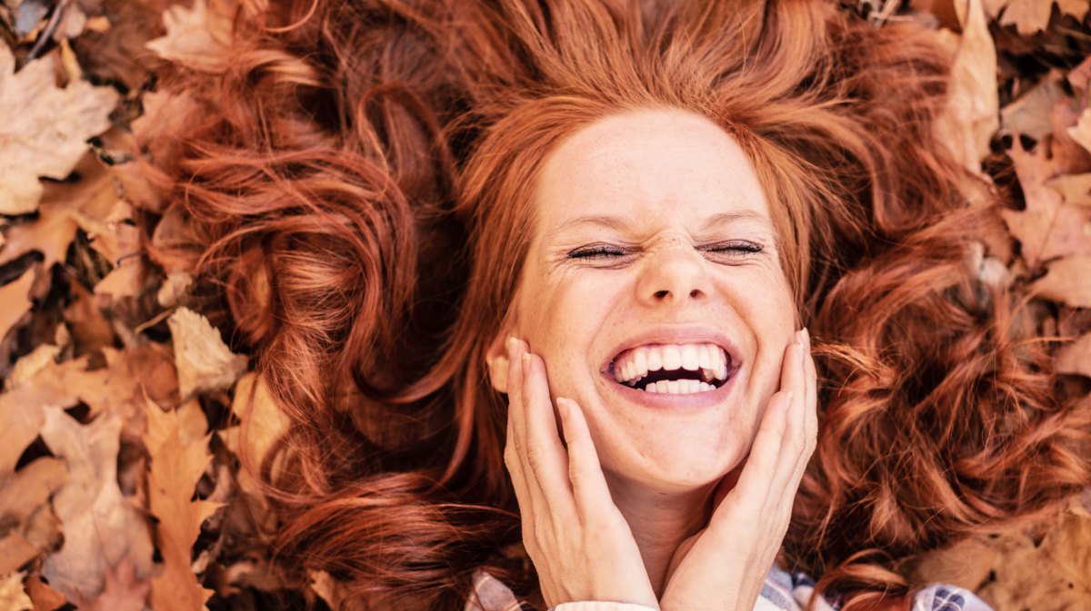 Frau mit roten Haaren liegt lächelnd im Herbstlaub