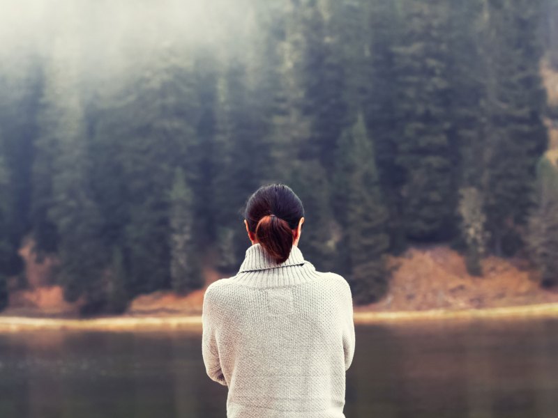 Frau steht an einem See mit Wald im Hintergrund