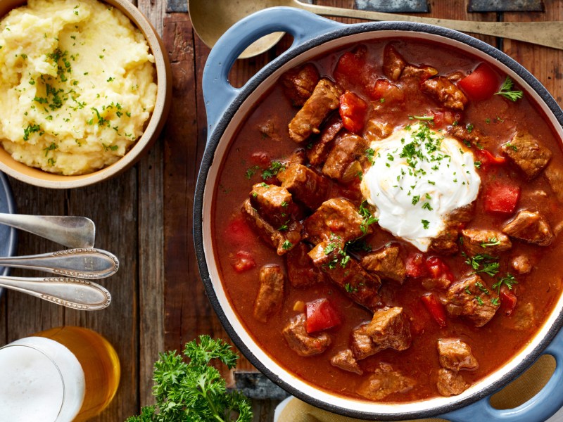 Gulasch und Kartoffelpüree auf rustikal gedecktem Tisch.