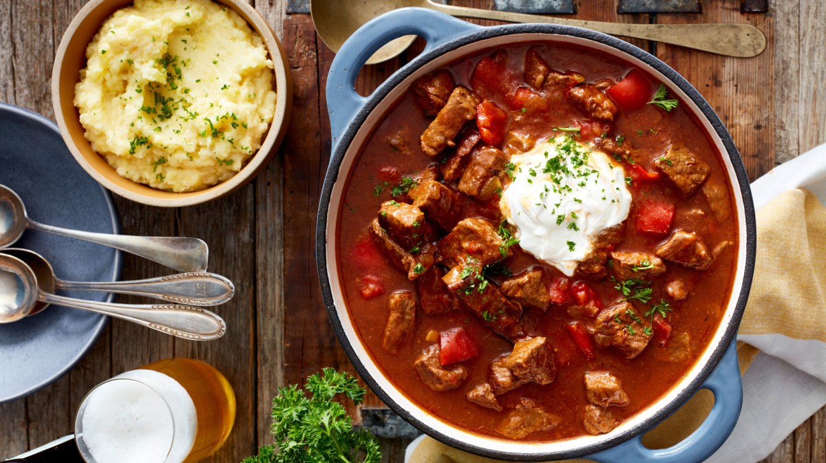 Gulasch und Kartoffelpüree auf rustikal gedecktem Tisch.